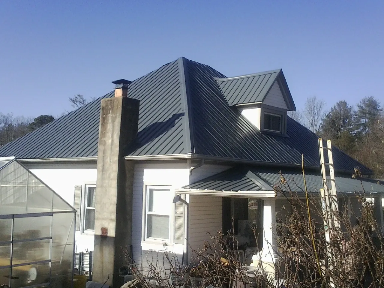 Dark blue standing seam metal roof on a white farmhouse with dormer — Slate & Tile Roof Repair by Roofing Brothers in Stratford