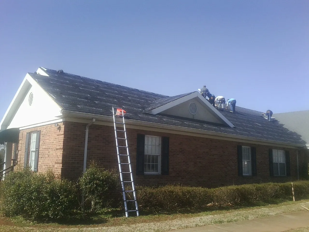 Crew tearing shingles off a brick ranch roof with a ladder set — Emergency Roof Repair work by our crew in Stratford