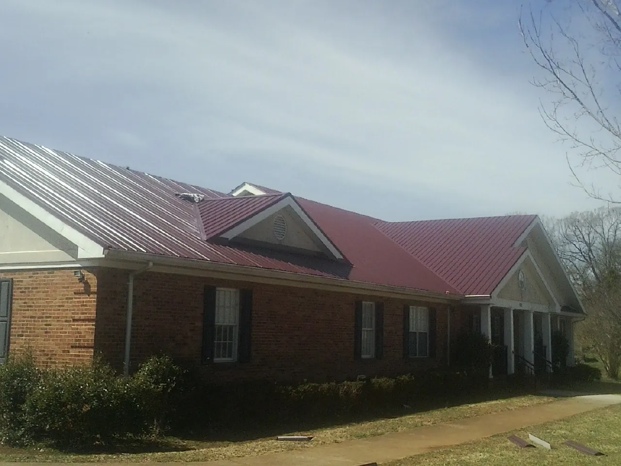 Red metal roof with gabled entries on a long brick building, from a Hail Damage Roof Repair job in Stratford